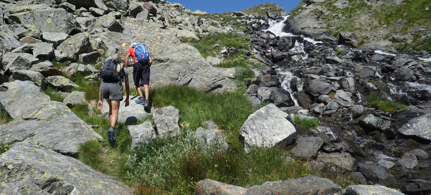 Salita lungo il torrente tra erba e sassi.